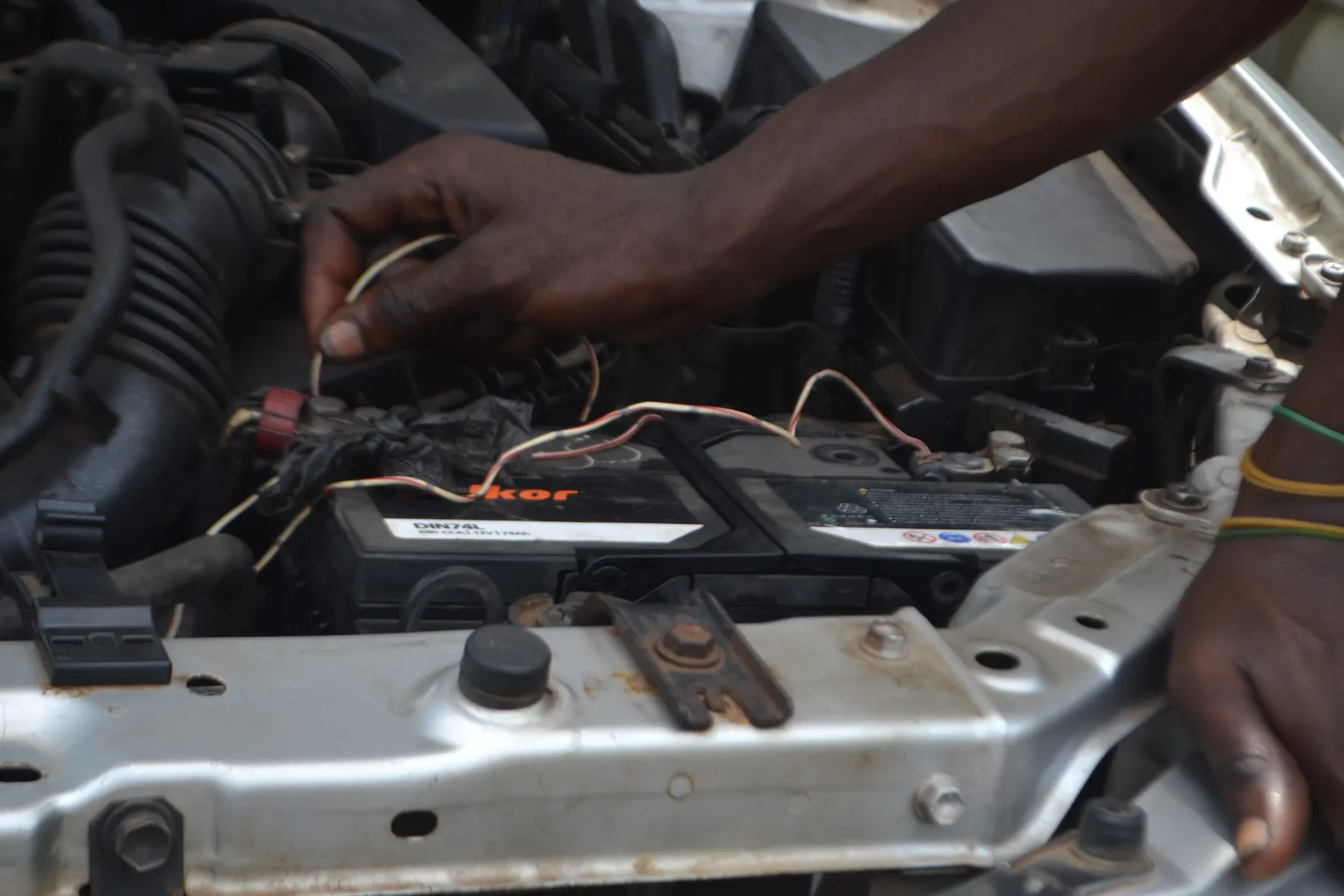 Hands checking battery terminals and wiring under the hood of a car