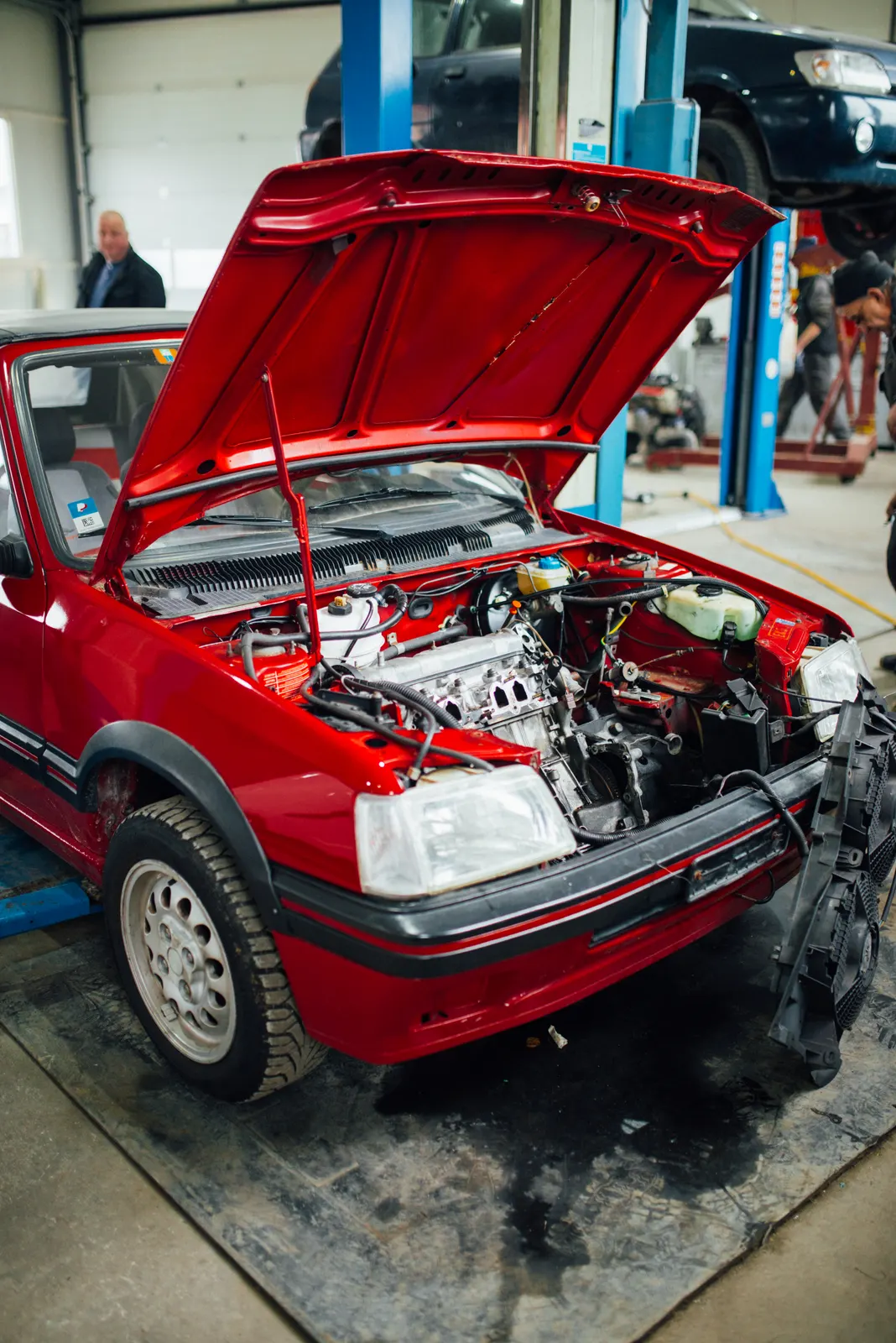 Car with its hood raised inside a service bay at a repair shop