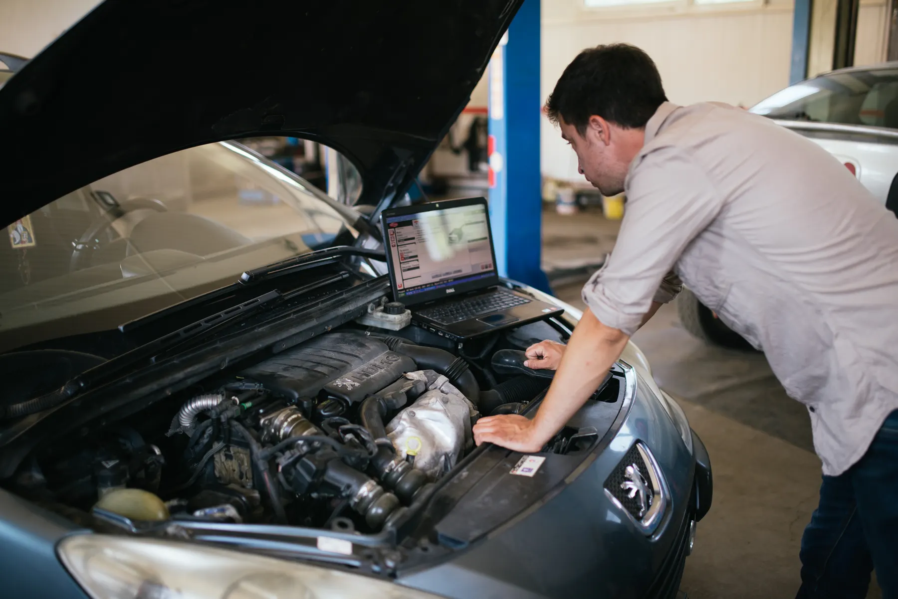 Technician reading live engine data on a laptop over an open hood in a repair bay