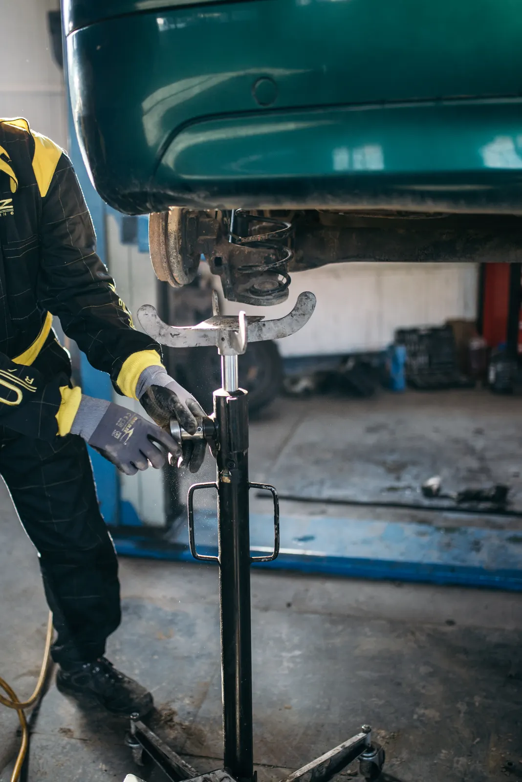 Technician in gloves working on a car suspension with the vehicle raised on a lift
