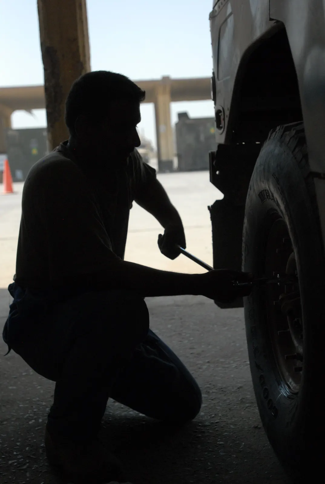 Technician kneeling beside a wheel with a wrench, silhouetted in a service bay